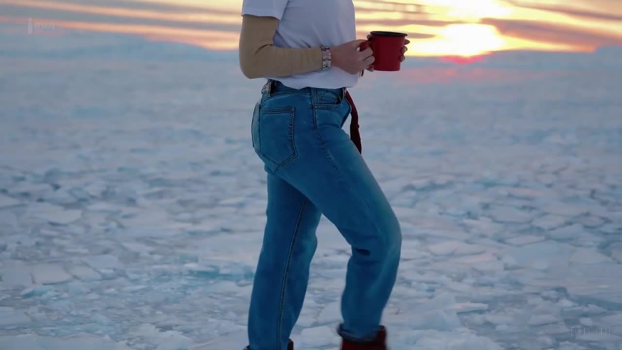 一个穿着蓝色牛仔裤和白色T恤的女人在南极洲美丽的日落时分愉快地散步。