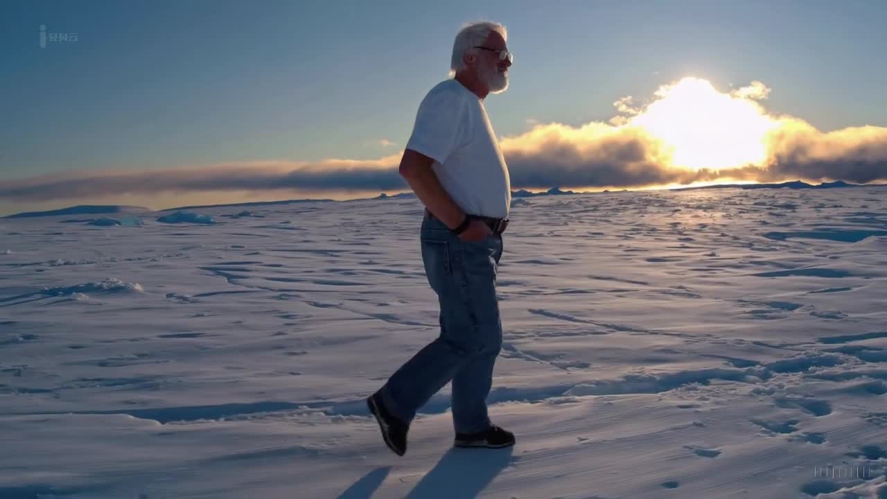 一个穿着蓝色牛仔裤和白色T恤的老人在南极洲美丽的日落时分愉快地散步。