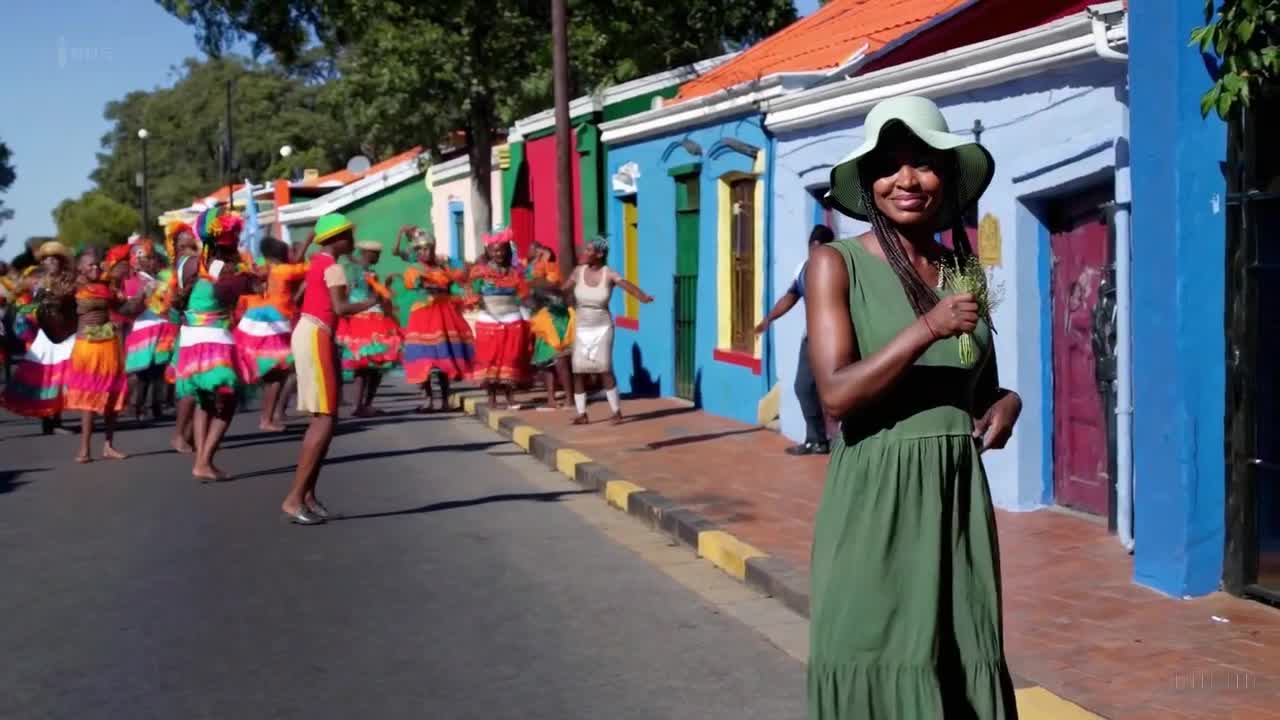 一个穿着绿色裙子和太阳帽的女人在南非约翰内斯堡举行的一场多彩节日中愉快地散步。