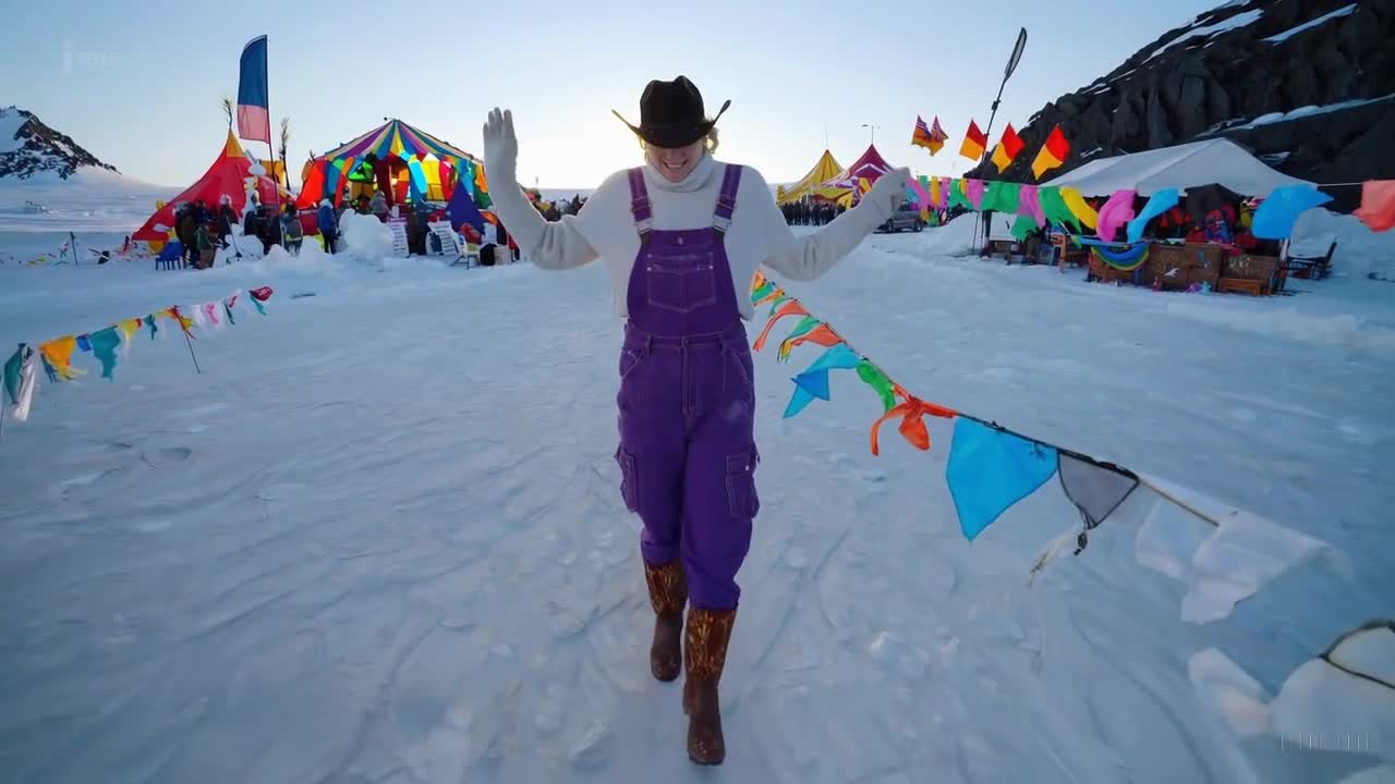 一个穿着紫色工装裤和牛仔靴的女人在南极洲举行的一场多彩节日中愉快地散步。